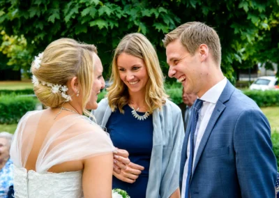 Brautpaar lacht mit Gast bei kirchlicher Hochzeit in St. Michael, Perlach. Hochzeitsfotografie in Muenchen.