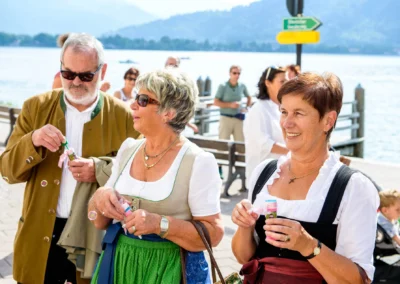 Gäste bei einer Hochzeit am Tegernsee, die Seifenblasen machen. Hochzeitsfotografie im Freien mit See im Hintergrund.