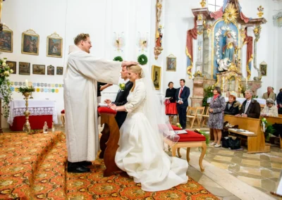 Brautpaar bei kirchlicher Trauung in St. Leonhard, Dietramszell, umgeben von Gaesten in bayerischer Kirche.