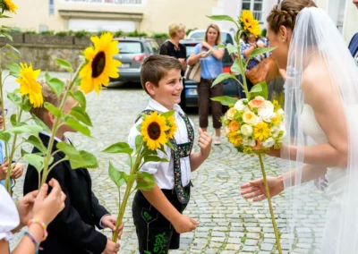 Junge mit Sonnenblume bei Hochzeit in Bad Toelz. Braut mit Blumenstrauss. Hochzeitsfotografie in Bayern.