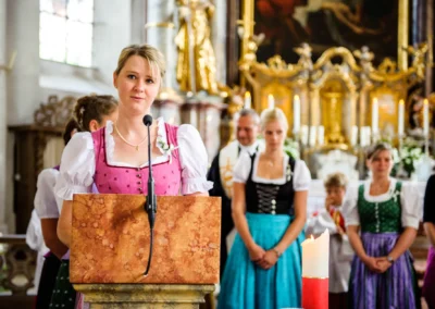 Kirchliche Trauung in Königsdorf, Frau im Dirndl am Rednerpult, Hochzeitsreportage, Kirche Dekoration im Hintergrund.