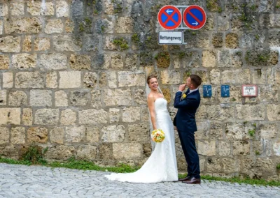 Brautpaar bei Hochzeitsportraits vor Steinwand in Bad Toelz. Braut in weissem Kleid, Bräutigam in dunklem Anzug.