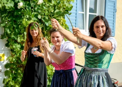Drei Frauen in Dirndl bei Hochzeit in Bayern halten Rosen hoch. Aufgenommen bei Hochzeitsreportage am Tegernsee.