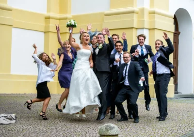 Jubelnde Hochzeitsgesellschaft bei kirchlicher Trauung in St. Michael, Pfanzeltplatz, Perlach. Hochzeitsfoto mit huepfen.