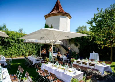 Hochzeitsreportage im Garten von Schloss Blutenburg in Muenchen, gedeckte Tische und Gaeste bei sonniger Trauung.