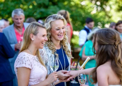 Gäste lachen mit Getränken bei Hochzeit im Schloss Blutenburg, München. Hochzeitsfotografie in Oberbayern.