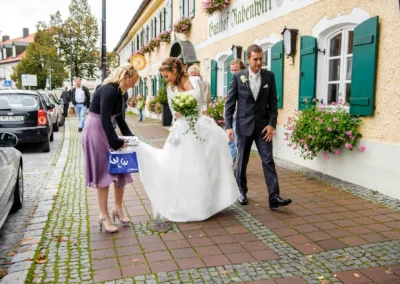 Brautpaar vor Gasthof Rabenwirt in Pullach, Hochzeitsreportage mit Braut in weissem Kleid und Brautigam in Anzug.