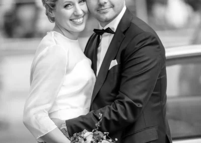 Brautpaar umarmt sich glucklich vor einem Auto in Rottach-Egern, Hochzeitsfotografie bei der Hochzeit.
