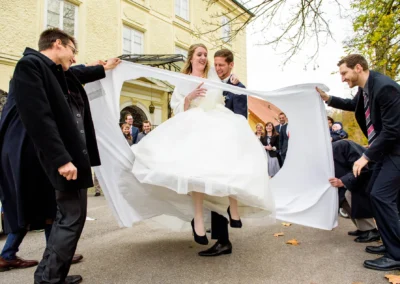 Brautpaar schneidet Herz in Laken bei Hochzeit in Bernried, umgeben von Freunden. Hochzeitsfotografie in Bayern.