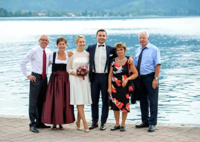 Brautpaar und Gaeste am Tegernsee vor dem Wasser. Hochzeitsfotograf aufgenommen bei einer Hochzeit.