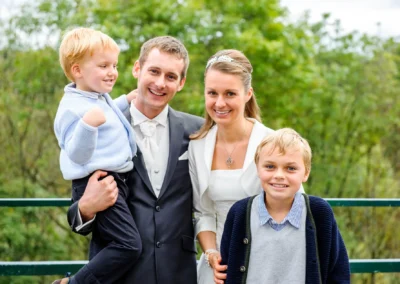 Brautpaar mit Kindern bei Hochzeit im Isartal, lachend vor gruenem Hintergrund. Hochzeitsfoto nah bei Pullach.
