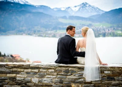 Brautpaar sitzt vor Bergkulisse am See, Hochzeitsfotografie Tegernsee.