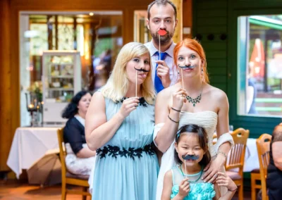 Gruppenfoto mit lustigen Requisiten auf einer Hochzeit im Wirtshaus am Rosengarten in Muenchen.