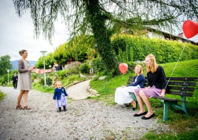 Hochzeitsfeier in Bad Wiessee mit Kindern auf einer Bank, rote Luftballons, festliche Stimmung im Freien.
