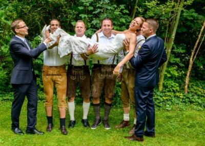 Hochzeitsfeier in Bad Tölz, Braut von drei Männern in Tracht auf einer Wiese bei Hotel Kolbergarten getragen.