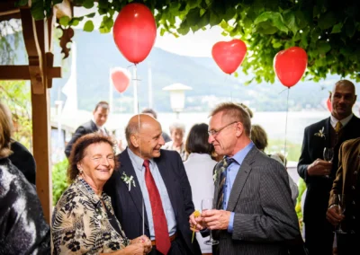 Hochzeitsfeier in Bad Wiessee am Tegernsee mit Gaesten, Luftballons und Bergkulisse im Hintergrund.