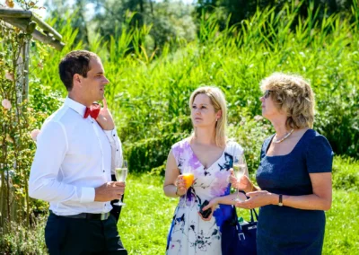 Hochzeitsreportage am Chiemsee: Drei Gaeste mit Getraenken, sonniger Tag, gruene Natur im Hintergrund.