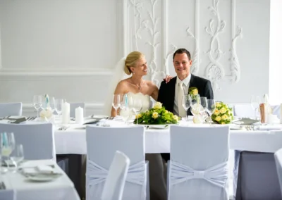 Brautpaar laechelt bei Hochzeitsfeier im Tegernsee Hotel; elegant gedeckter Tisch mit Blumen und Kerzen.