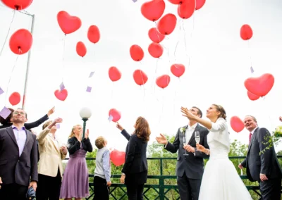 Hochzeitsfoto in Pullach: Menschen lassen bei einer Hochzeit Herzluftballons steigen, Brautpaar und Gaeste schauen zu.