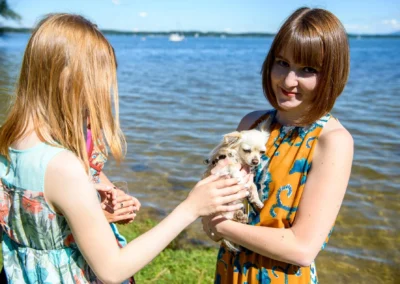 Zwei Frauen mit Hund am Ufer des Chiemsees bei einer Hochzeit; entspannte Sommer-Hochzeitsreportage in Oberbayern.