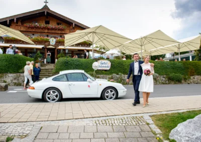 Brautpaar vor dem Seehotel Malerwinkel bei Hochzeit in Rottach-Egern, weisser Porsche im Vordergrund, Hochzeitstag.