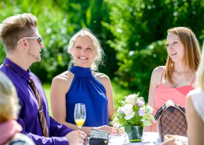 Gaste bei einer Hochzeit im Chiemgau, lachen und unterhalten sich im Freien mit Blumen und Getraenken, perfekte Reportage.