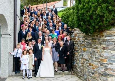 Hochzeitsgruppe bei Feier im Tegernsee Hotel, festlich gekleidete Gaeste vor Natursteinwand, suedlich von Muenchen.