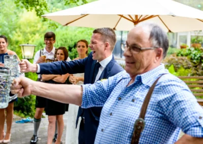 Gäste heben Bierkrüge bei Hochzeitsfeier im Hotel Kolbergarten, Bad Tölz. Hochzeitsfotografie aus Bayern.