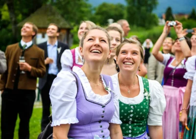 Personen in Tracht bei Hochzeitsfeier im Terrassenhof, lachen und blicken nach oben, Bad Wiessee, suedlich von Muenchen.