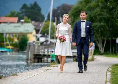 Brautpaar spaziert am Tegernseeufer, sie lacht beim Hochzeitsfotoshooting in Rottach-Egern.