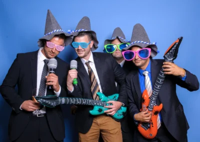 Hochzeit in Oberbayern: Vier Maenner mit bunten Brillen, Schaumstoffgitarren und Hueten feiern den besonderen Tag vor einer Fotobox.