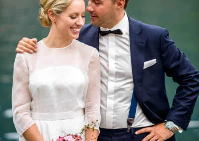 Brautpaar am Tegernsee, er lacht, sie mit Blumenstrauss, Hochzeitsfoto im Anzug und Kleid, Hochzeit bei Seehotel Malerwinkel.