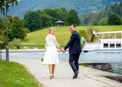 Brautpaar spaziert Hand in Hand am Tegernseeufer, Hochzeitsfoto in Rottach-Egern.
