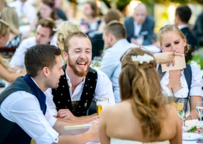 Gäste lachen bei der Hochzeit in Schloss Blutenburg, Oberbayern. Hochzeitsreportage in fröhlicher Atmosphäre.