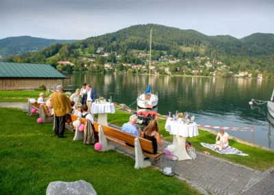 Gäste genießen eine Hochzeitsfeier am Tegernsee mit Blick auf Boote und Berge. Hochzeitsfotografie im Freien.