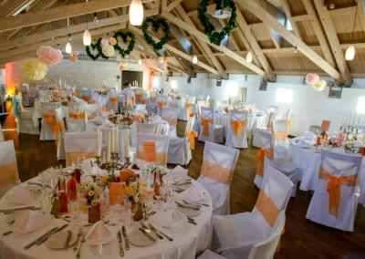 Festlich dekorierter Hochzeitssaal in Obermenzing mit runden Tischen, Kerzen, Blumen und orangenen Schleifen.