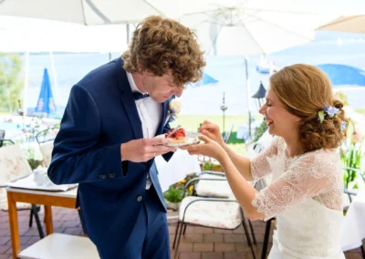 Brautpaar teilt Kuchen bei Hochzeit am Chiemsee, Unter freiem Himmel mit Seeblick, Hochzeitsreportage.