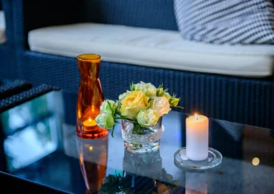 Kerze und Blumenarrangement auf Glasstisch bei Hochzeitsfeier im Hotel Kolbergarten in Bayern. Hochzeitsfoto.