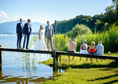 Hochzeitsreportage am Chiemsee: Brautpaar und Trauzeuge auf Steg mit malerischem Alpenhintergrund in Oberbayern.
