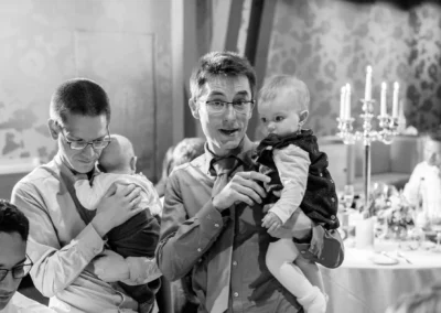 Zwei Maenner mit Kindern bei Hochzeitsfeier in Bernried. Hochzeitstisch im Hintergrund. Hochzeitsfotografie in Bayern.