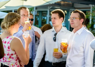 Hochzeitsgesellschaft am Chiemsee. Vier Gaeste mit Getraenken bei sonniger Feier im Malerwinkel aufgenommen.