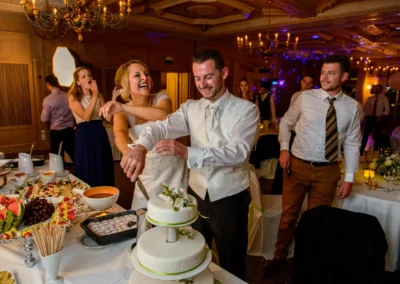 Brautpaar schneidet Hochzeitstorte bei Feier nahe München, fröhliche Momente festgehalten in Hochzeitsreportage.