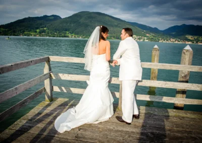 Brautpaar auf Steg am Tegernsee mit Blick auf Berge, aufgenommen bei Hochzeitsfeier in Bad Wiessee.