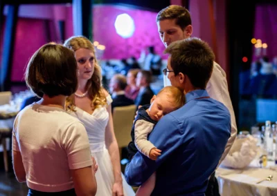 Gruppengespräch bei Hochzeitsfeier, schlafendes Baby in Bernried. Hochzeitsreportage zeigt herzliche Momente.