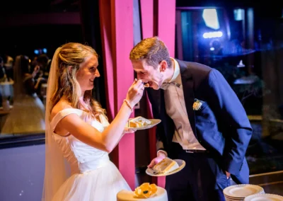 Brautpaar bei Hochzeitsfeier im Marina Resort Bernried, Braut fuettert Bräutigam mit Kuchen, Hochzeitsfotografie.