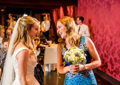 Braut und Gast im Gespraech bei Hochzeitsfeier in Bernried. Romantische Hochzeitsfotografie mit Blumenstrauss.