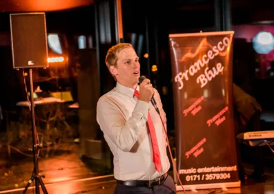 Mann singt bei Hochzeitsfeier im Marina Resort, Mikrofon in der Hand, im Hintergrund Banner und Lautsprecher.