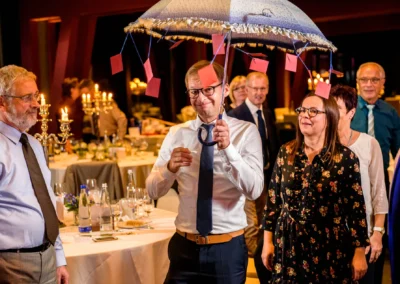 Personen feiern bei Hochzeit in Bernried, Mann mit dekorativem Regenschirm. Hochzeitsreportage zeigt fröhliche Gäste.