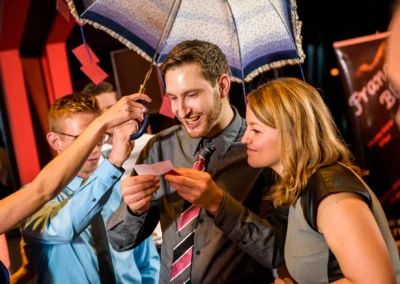 Menschen feiern auf einer Hochzeit im Marina Resort, lachen und lesen Notizen unter einem Regenschirm. Hochzeitsreportage.