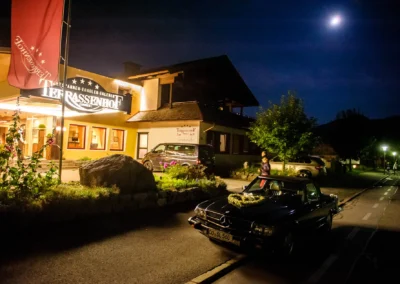 Nachtaufnahme einer Hochzeit im Terrassenhof, Bad Wiessee. Beleuchtetes Hotel und dekoriertes Auto unter Mondlicht.